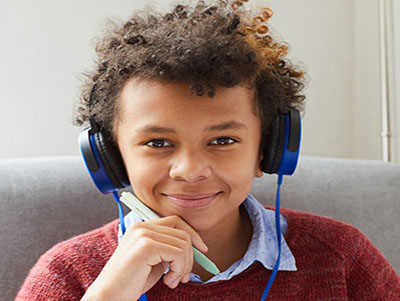 Portrait of African boy with curly hair in headphones listening to music and smiling at camera